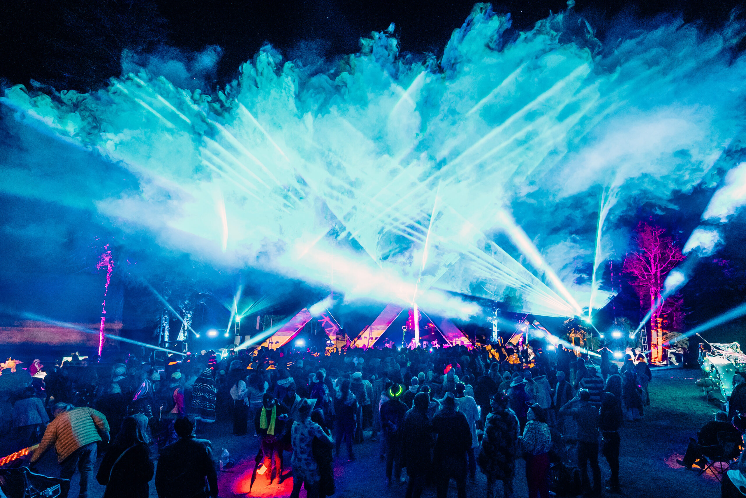 dark sky illuminated by bright blue lights and lasers over a crowd at outdoor music festival