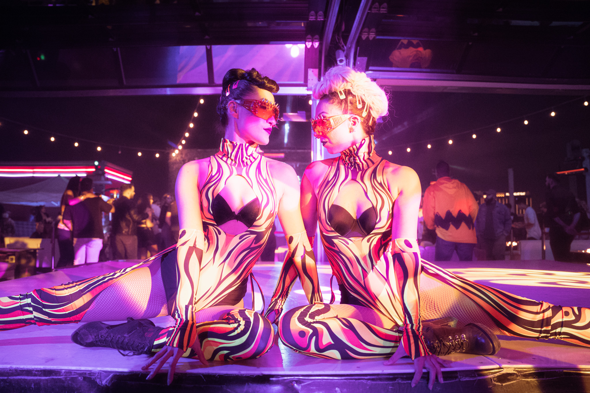 las vegas go go dancers dressed in vibrant tiger striped jump suits staring into each others eyes