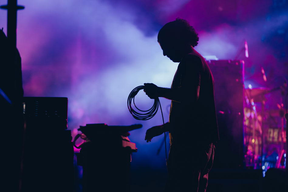 Production team member holding cables backstage under vibrant lighting at music event
