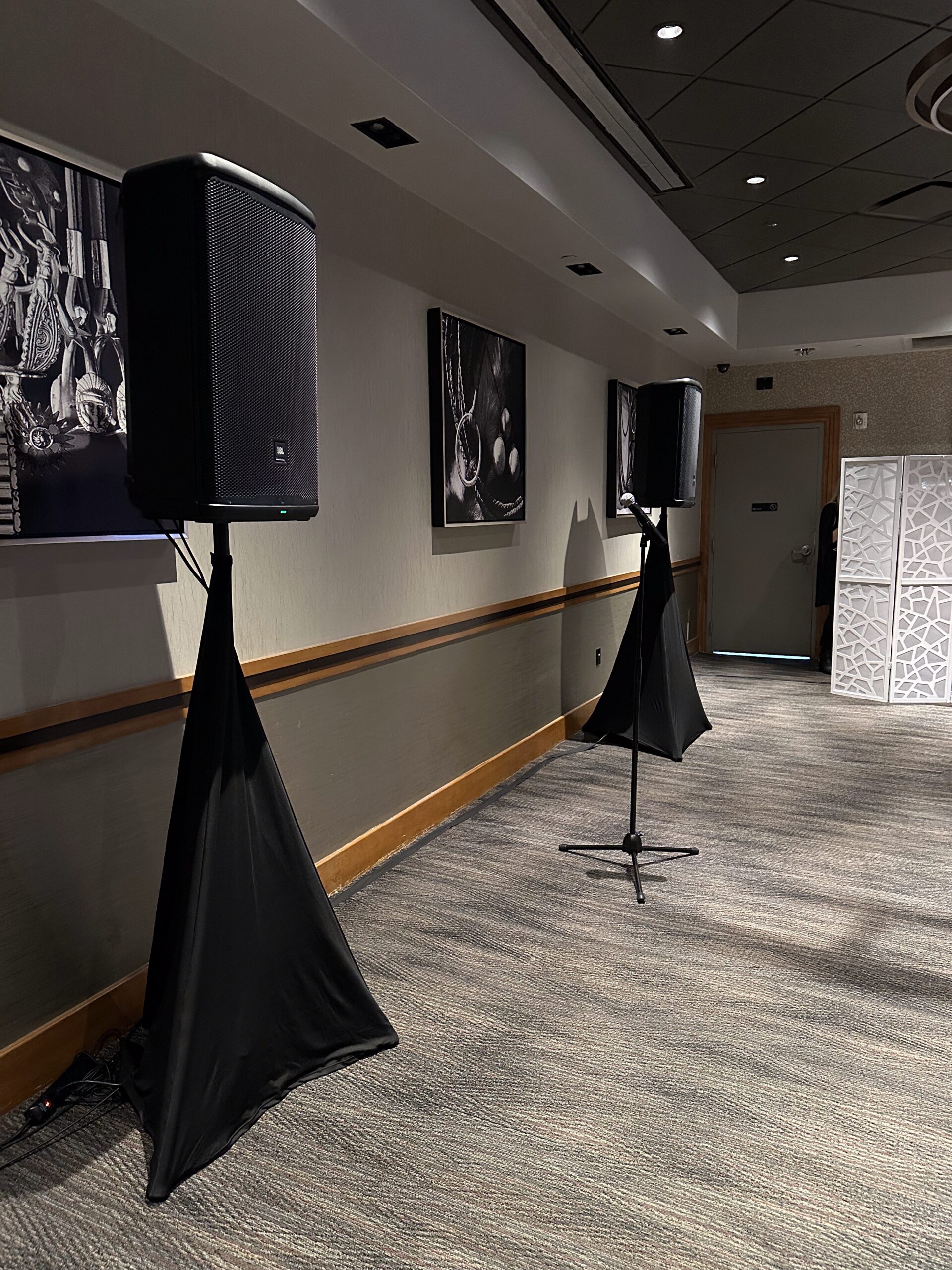 Two JBL speakers on stands with microphone setup for small indoor event